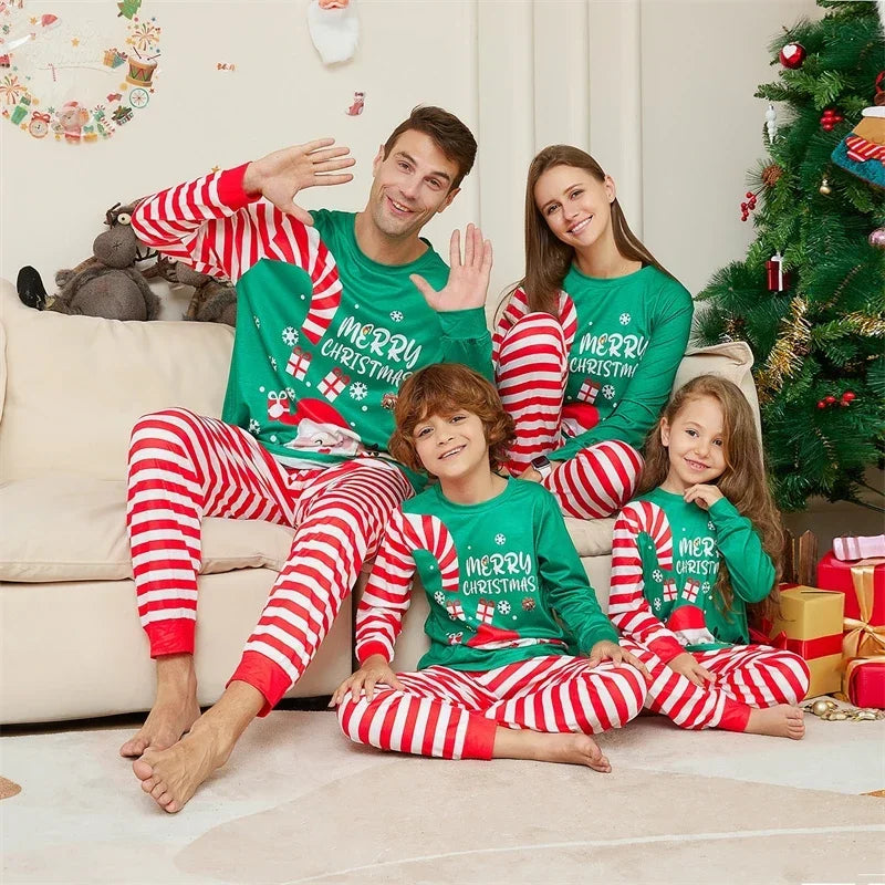 Parents and kids posing in matching candy cane pyjamas by a decorated Christmas tree.